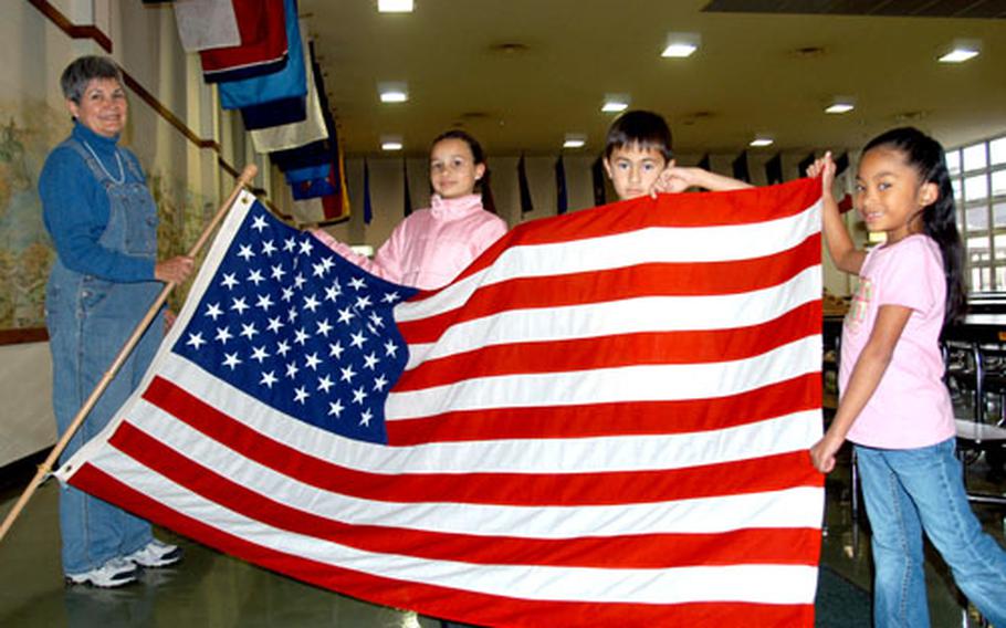 Sollars Elementary School second-grade teacher Elise Henderson and three of her students from last year — from left, Ryann Moyers, Ryan Seau and Tamiyah Kunsman — hold up the U.S. flag Thursday after helping decorate the Misawa Air Base school cafeteria with 50 state flags, the culmination of a two-year class project led by Henderson.