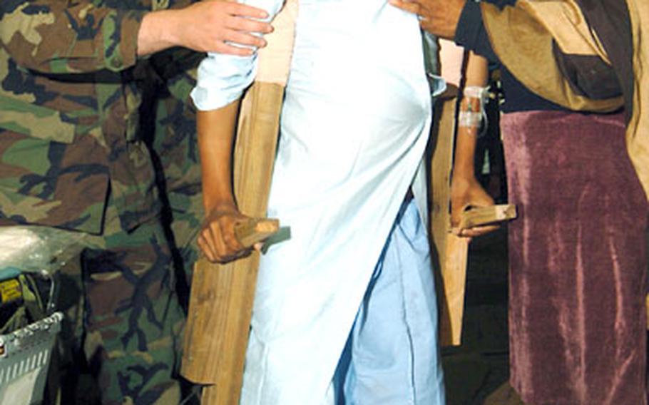 A Pakistani boy with a broken leg, helped by Cpl. Andrew Woughter and the boy's mother, tries out his new crutches, built by a U.S. Navy Seabee.