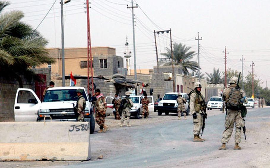 U.S. Marines watch over a cadre of militia members from the Katab Al Hamsa. The militia members are waiting outside a Marine base in Husaybah while their leader meets with U.S. and Iraqi leaders inside. U.S and Iraqi leaders are urging the militia leader to disarm.