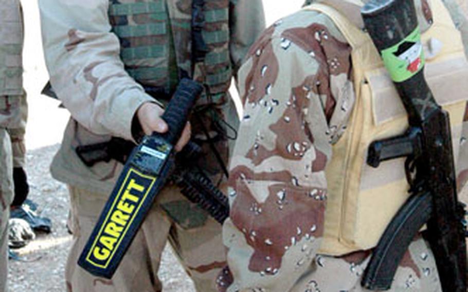 Sgt. Brian Griggs, of Fox Troop, Sabre Squadron, 3rd Armored Cavalry Regiment hands a metal detector to an Iraqi army soldier on Tuesday after demonstrating how to use it at the Rawabi School polling site in Tal Afar.