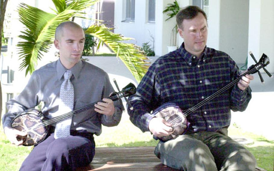 Jonathan Beyer, left, and Jay Schwarzmann play the Okinawan sanshin Monday under a gazebo at the Department of Defense Dependents Schools Pacific building on Torii Station.
