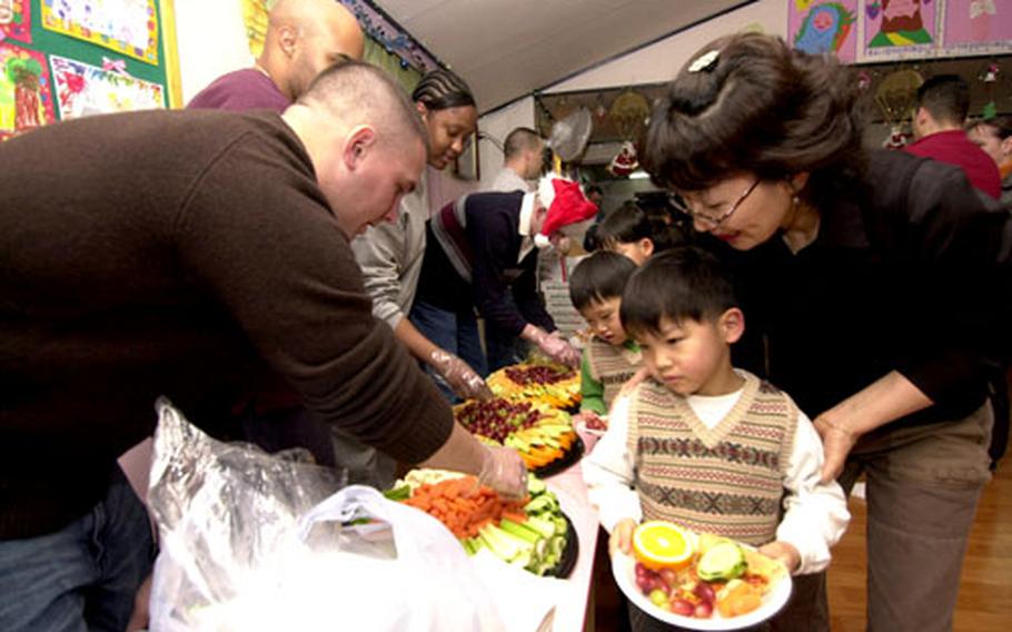 Capt. Nicholas Bugajski, of 8th Military Police Brigade’s Headquarters and Headquarters Company, serves food to kids at the Sung Ro Won orphanage during a holiday party Thursday night.
