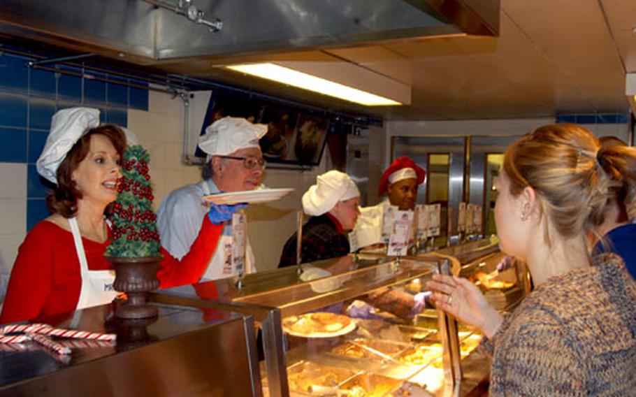Maria Tuttle hands a plate of food to an airman at RAF Lakenheath’s dining facility Christmas morning while her husband, U.S. Ambassador to the United Kingdom Robert Tuttle, prepares a plate for another airman.
