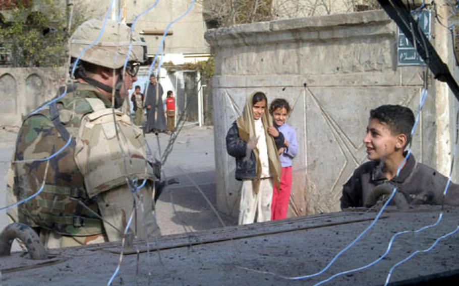 Spc. Michael Johnson talks to an Iraqi boy as soldiers from Company A, 2nd Battalion, 14th Infantry Regiment, patrol a Baghdad neighborhood during the elections. The picture was taken through Johnson&#39;s Humvee&#39;s cracked winshield, which was damaged that morning when a mortar landed nearby.