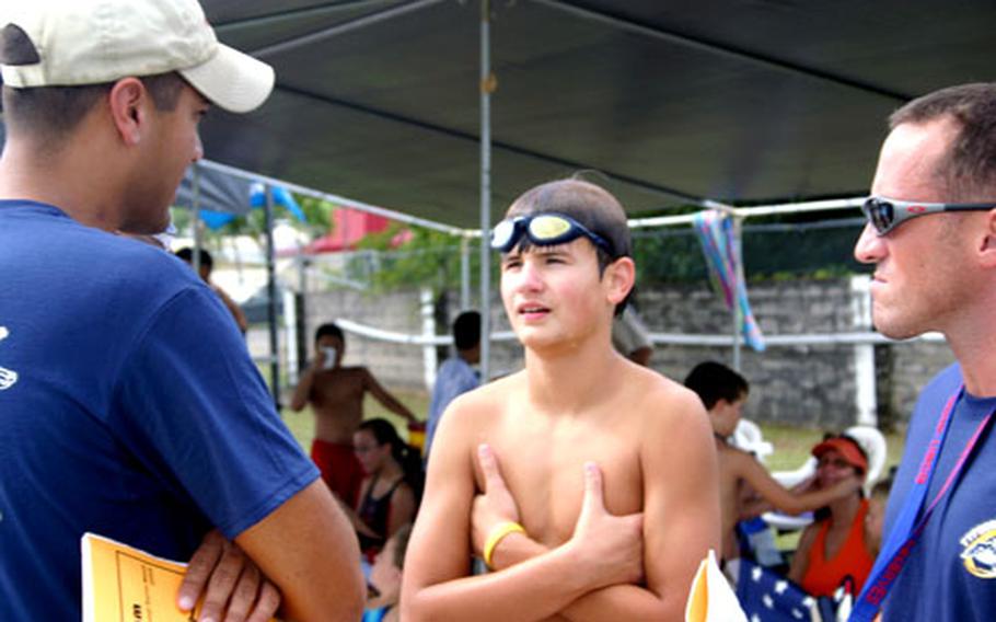 Swimmer Austin Barnett, 12, discusses a just-completed race with U.S. Naval Base Guam Typhoons head coach Gopi Nadella, left, and assistant coach Francis Johnson, right, during a competition at the Agana Pool on Guam on Dec. 27. Both volunteer coaches are active-duty sailors stationed on Guam.