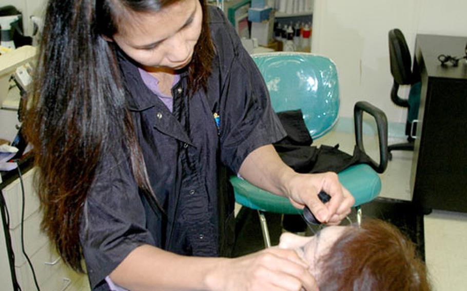 Hair stylist Josephine Crown uses a technique called threading to shape Yoko Ohta’s eyebrows Thursday at Sasebo Naval Base, Japan.