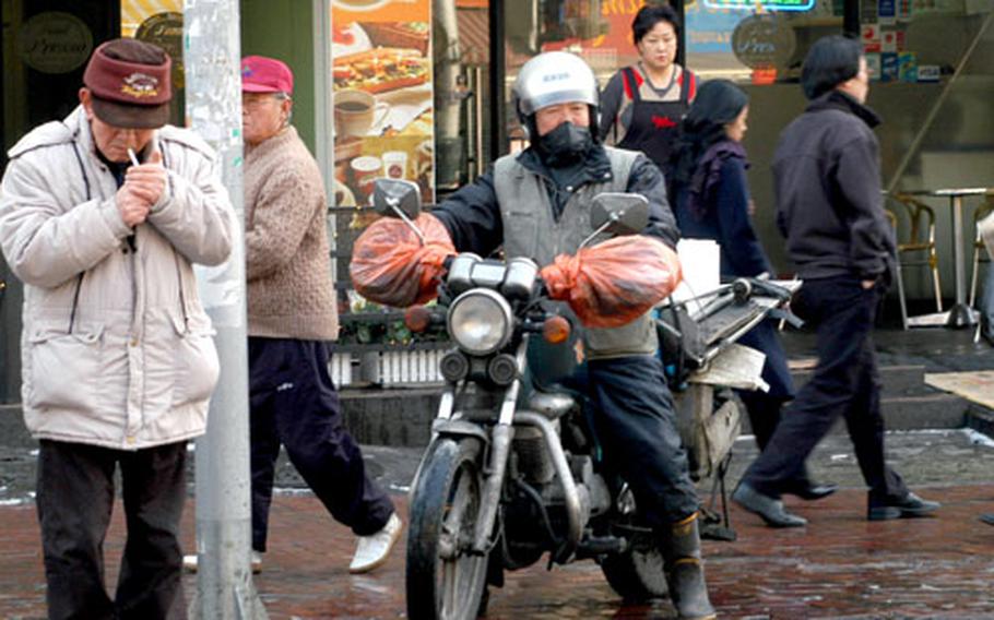 A motorcyclist waits on the sidewalk with pedestrians in Seoul, a common sight in a country rated as one of the worst for vehicle accidents.