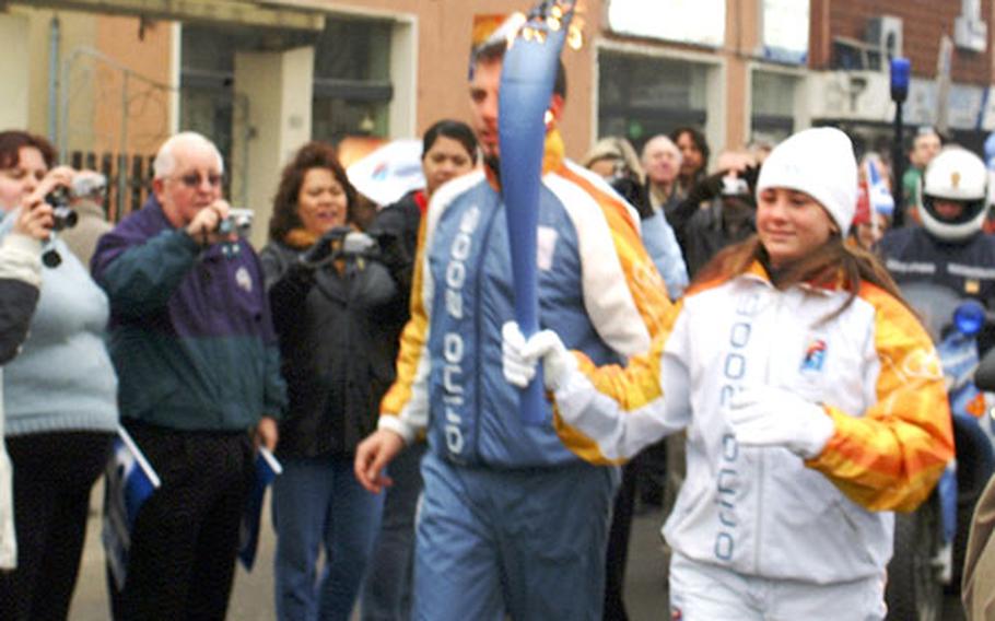 The Olympic torch passed in front of Caserma Ederle in Vicenza, Italy, on Tuesday, and hundreds of Americans got up early and braved a few snowflakes to see it pass by. Some waited for about an hour to watch the display, which ran a bit behind schedule. The torchbearer was preceded by several vehicles, including a few carrying small flags bearing the logos of sponsors Samsung and Coca-Cola.