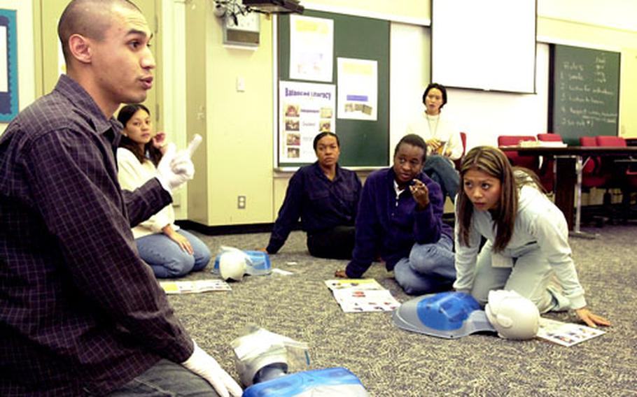 Marine Staff Sgt. Pablo Mendoza, left, a volunteer instructor for the American Red Cross, demonstrates how to sweep clean a victim’s mouth during cardiopulmonary resuscitation training for staff members Friday at Kinser Elementary School on Camp Kinser, Okinawa.