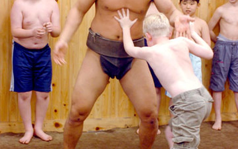 A Camp Zama Cub Scout tries — and tries — to shove a professional sumo wrestler out of the ring on Saturday at the Arashio Sumo Stable in Tokyo.