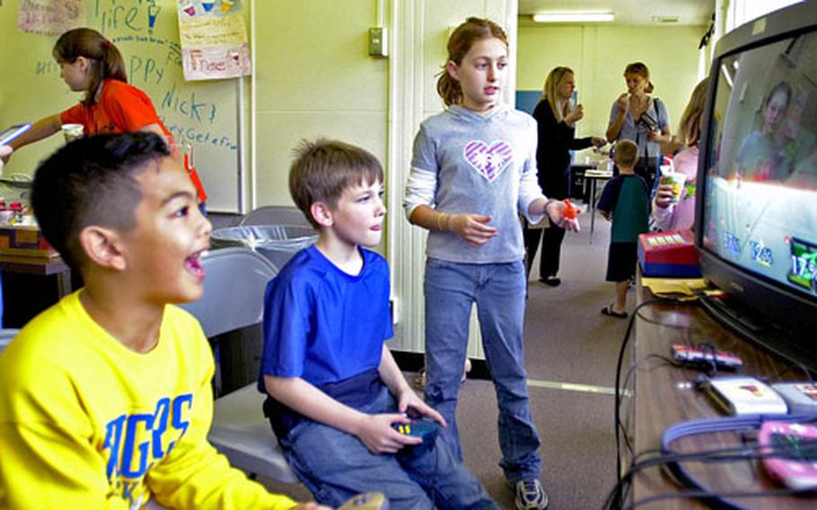 Isabel Hagopian, right, watches as Ricky Arellano, left, and Peter Trusty play video games at her “business” at Stearley Heights Elementary School on Kadena Air Base. The third- and fourth-grade multi-age classes at the school currently are taking part in a “mini-society” economics program in which they create their own businesses and run them.