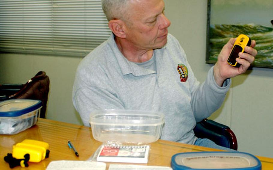 Walter Birkenheier, Sasebo Naval Base’s Sailing and Outdoor Recreation Center manager, displays the contents of a cache like the nine he’s already placed in locations around Kyushu. The boxes contain a logbook, pencil, key chain and stash notes inside. When geocache players find the cache, they register in the logbook, leave a note, add to the cache and replace it for another player to find using a GPS device, such as the one Birkenheier is holding.