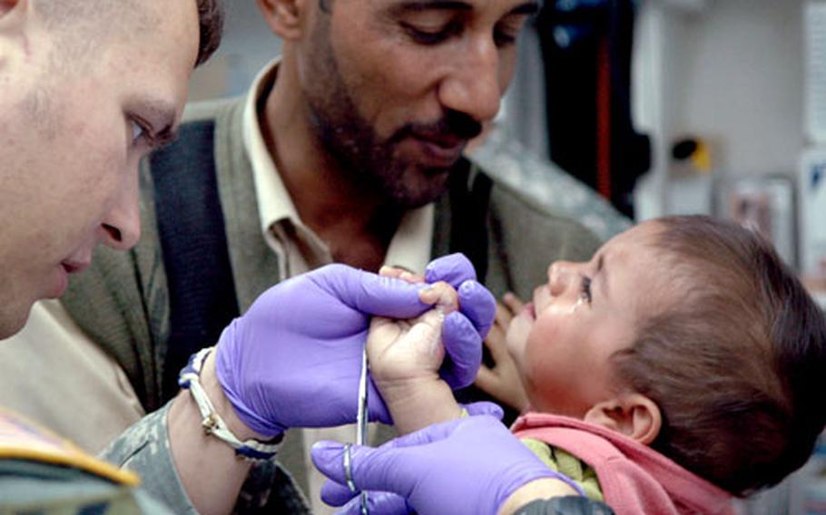 Spc. Carl Jackson, left, cleans a burn on a young Iraqi girl’s hand on Friday at a free clinic at Camp Scania, Iraq. She is comforted by an unidentified man. Each day, the clinic treats between 40 and 60 patients, who suffer from everything from a common cold to rare diseases.