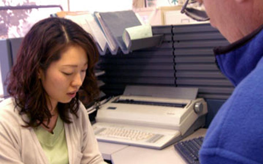 Tomoko Shimozono, an employee at Yokosuka Naval Base’s Vehicle Registration Office, assists a customer. The office will start facilitating 2006 Road Tax payments this Thursday and Friday and again Apr. 5-7. Taxpayers first will pay at the base’s Fleet Theater, then pick up a decal across the street at the VRO.