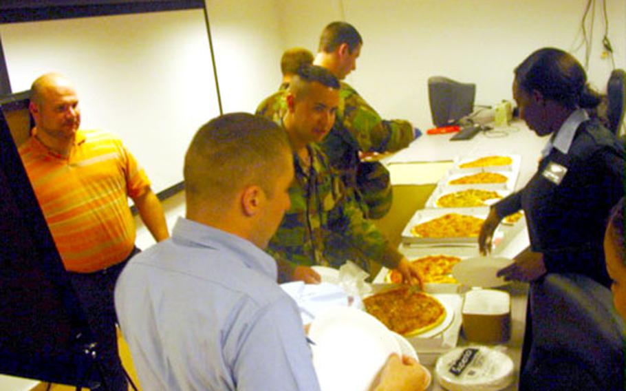 Eric Uzelac, left, Liberty Program coordinator for Naval Station Rota, Spain, watches as sailors from the base Supply Department help themselves to pizza during the March 23 pizza party and Liberty Program presentation.