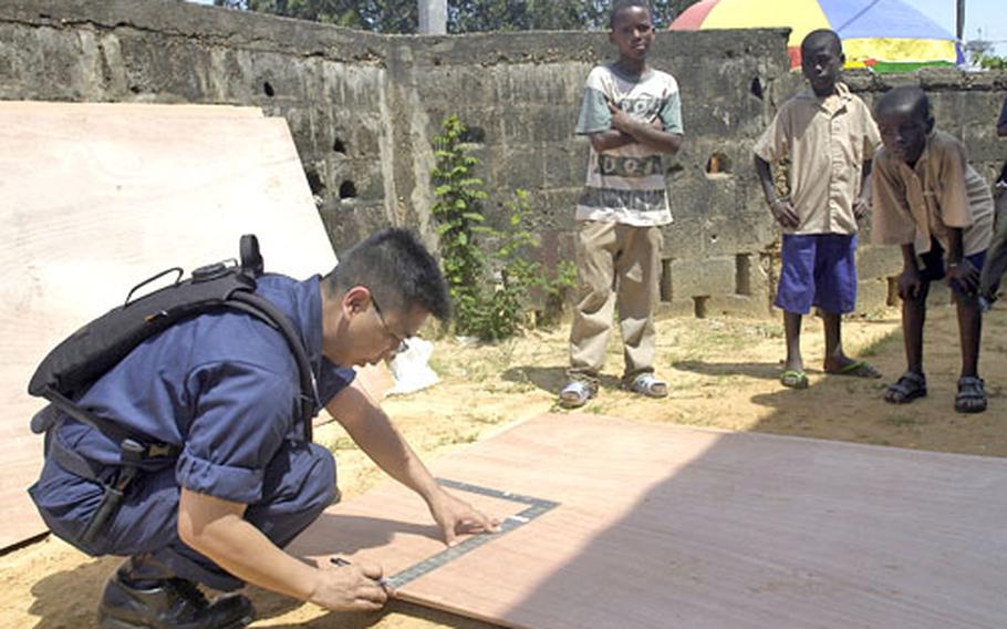 Students of the Jean Felix Tchicaya Primary School in Pointe Noire, Republic of Congo, watch as Petty Officer 1st Class Vincent Abellera, a hospital corpsman with the USS Emory S. Land, works during a community relations project.