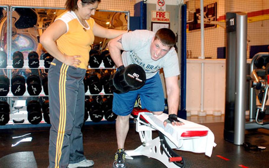 Raquel Cruz, a fitness assistant intern at the Morale, Welfare and Recreation Fleet Fitness Center at Sasebo Naval Base, Japan, reminds Petty Officer 3rd Class Joseph Belt to maintain a safe and proper form while lifting weights.