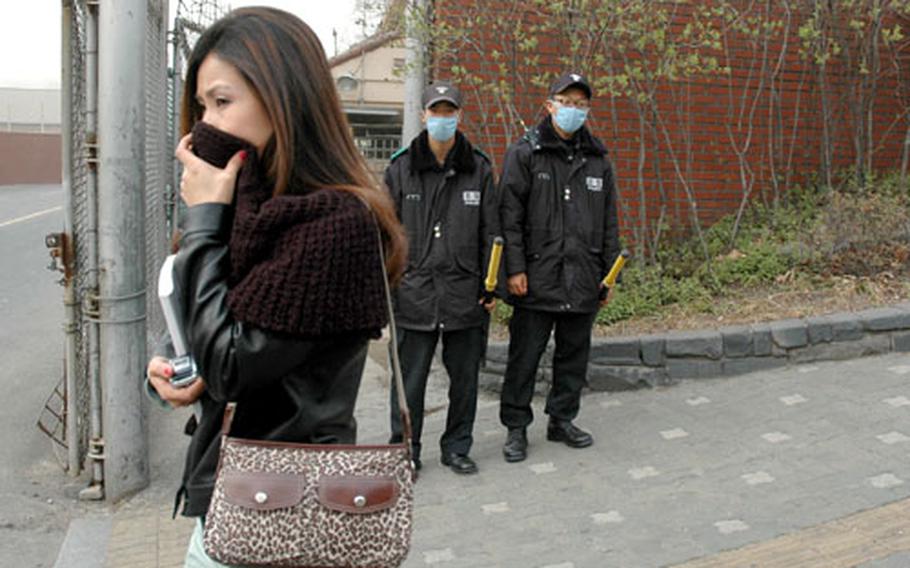 A woman walks in front of a gate to Yongsan Garrison shortly after 5 p.m. Saturday, shielding her nose and mouth from the dangerously high levels of yellow dust blanketing the city.