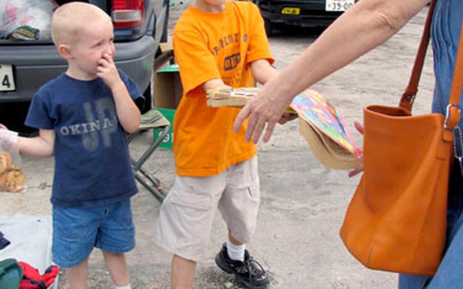 Taylor Bowman, 9, sells a handful of coloring books for 100 yen, while his brother, Thomas, 4, watches at a flea market at Camp Foster, Okinawa, on April 1.
