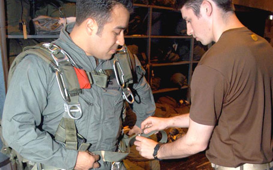Senior Airman Robert Gutierrez, left, rigs up his parachute gear with help from Senior Airman Dale Young, both combat controllers with the 321st STS, inside the squadron&#39;s hangar on RAF Mildenhall.