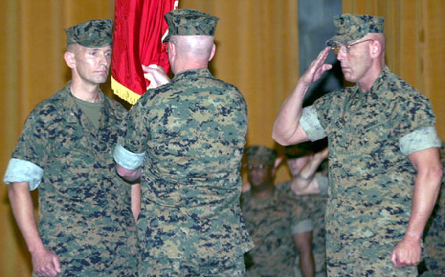 Col. Walter L. Miller Jr. hands the 31st Marine Expeditionary Unit colors to Col. John L. Mayer, left, during a change of command ceremony at the base theater at Camp Hansen on Thursday. Mayer, a Dallas native, assumed command over the unit. Miller will transfer to U.S. European Command as the assistant chief of staff.
