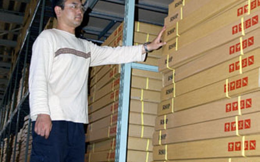Masato Shimamura, Furnishings Management Office repair shop and warehouse section supervisor at Misawa Air Base, Japan, stands by stacks of satellite dishes, unused and still in their boxes. The base has just over 1,000 satellite dishes and about 700 decoders available.