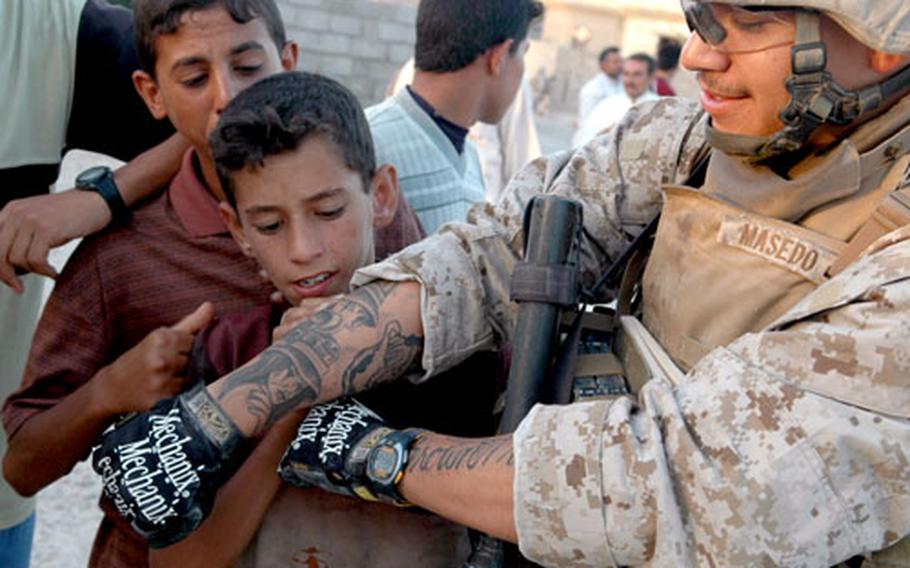 Marine Pfc. Oscar Masedo, 20, of San Marcos, Calif., shows his tattoos to Iraqi boys during a recent patrol north of Fallujah, in western Iraq. ¶ See more photos .
