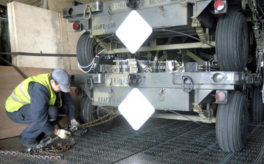 An aircraft crewmember tightens down a stack of trailers before deployment.