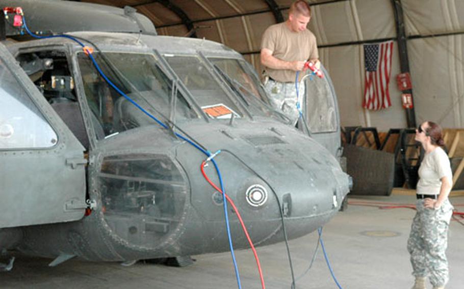 Army Spc. Brad Verzweyvelt and Spc. Stephanie Magnus of the 277th Aviation Support Battalion work on the electrical system of a UH-60 Black Hawk at a repair hangar in Bagram Air Base, Afghanistan, in this undated file photo. Other members of the repair crew posted the “For sale” sign in the window shortly before work began, and joked with passers-by about giving it away for a mere $500.