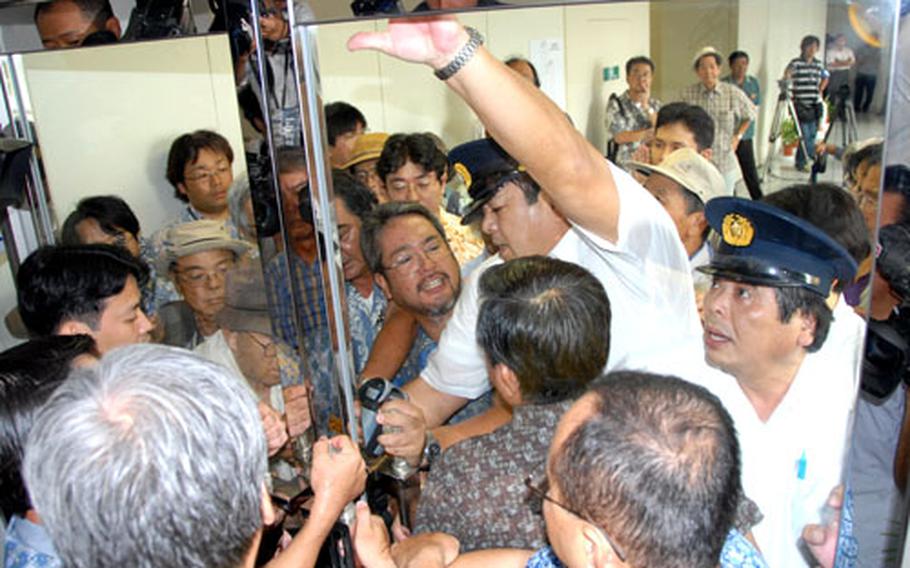 Two security guards block the door from one side while prefectural government employees help from the other side to keep about 30 protesters from barging into a Thursday meeting between Japanese defense official Iwao Kitahara and Okinawa Gov. Keiichi Inamine.