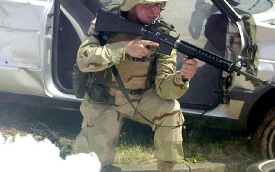 A soldier takes a knee by the shell of a car during a simulated mission at Baumholder&#39;s new training facility.