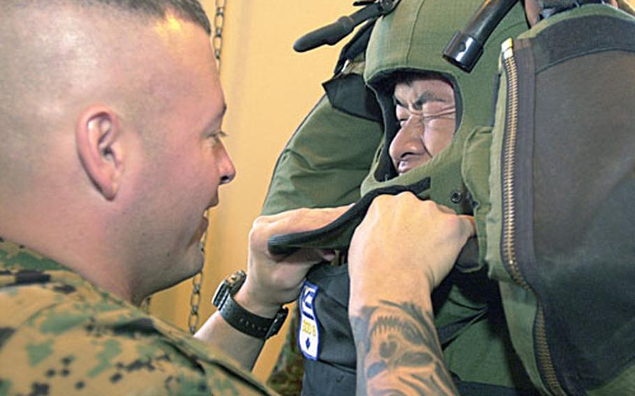Staff Sgt. Nathaniel Corsby straps Sgt. Kazuhide Daeda, a Japanese Self Defense Force soldier, into an 85-pound explosive-ordnance-disposal-8 bomb suit.