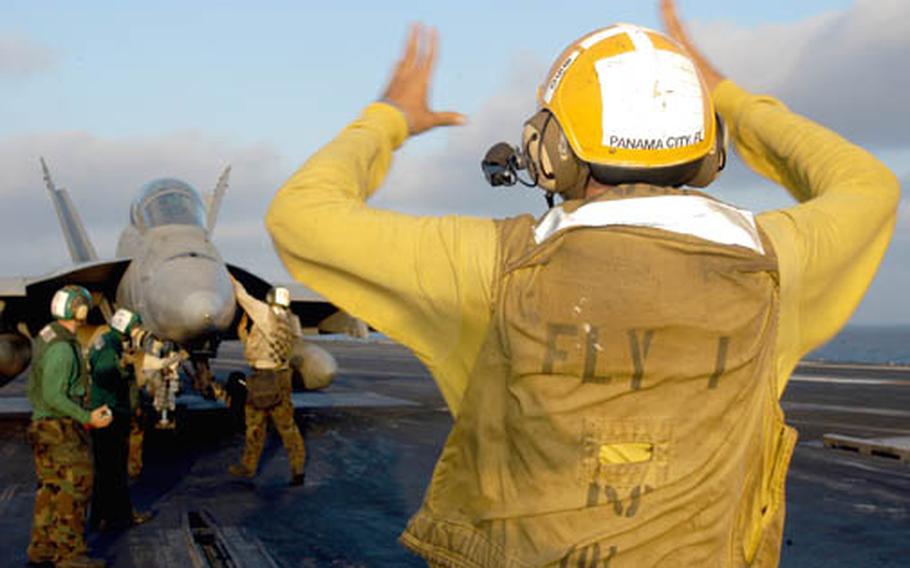 Airman Brian Kuhaneck, aircraft director on catapult 2 aboard the USS Enterprise, directs an F/A-18 Super Hornet getting ready to launch from the carrier on its way to Afghanistan.