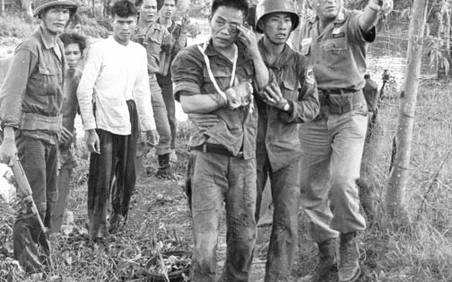 Maj. Robert M. Campbell, right, an American adviser from Fayetteville, N.C., points the way to a helicopter that will bring a wounded Vietnamese ranger, at center, to a hospital. The soldier lost part of his right hand to a Viet Cong booby trap.