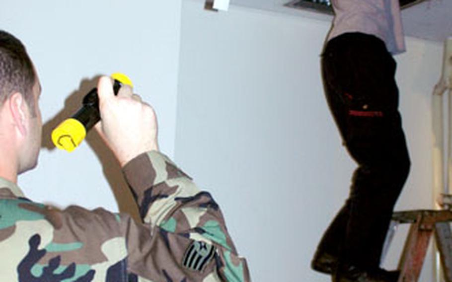 An airman shines a flashlight into a hole in the ceiling of the Airman and Family Readiness Center at Yokota Air Base while a Japanese worker investigates the damage caused by a broken water pump.