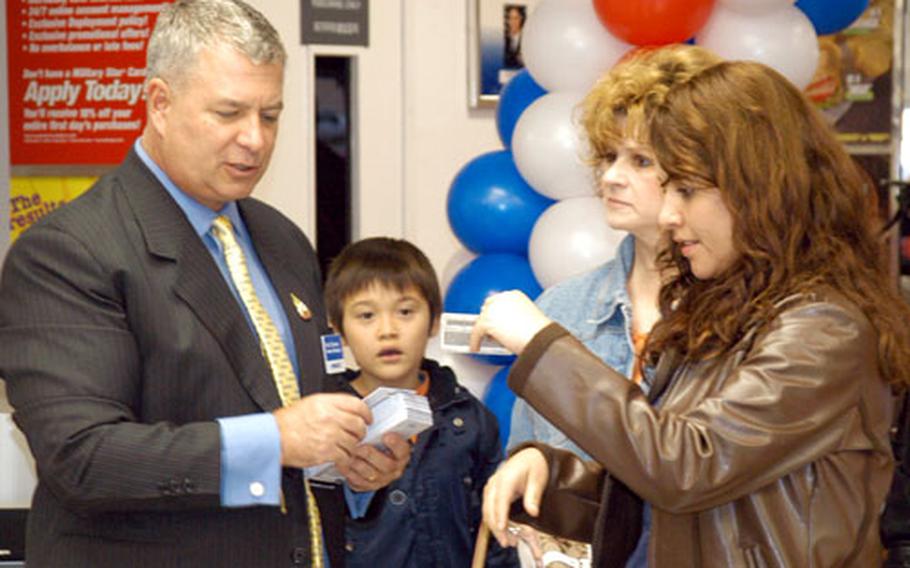 During the grand opening of the Camp Walker PX Nov. 18, Kurt Brunen, Area IV general manager for AAFES in Daegu, hands a $20 AAFES gift certificate to Sandra Medler, wife of 1st Lt. Ty Medler of the 168th Medical Battalion.