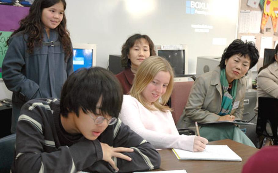 Joseph Park reads his writing assignment aloud in Steve Kennedy’s language arts class at Seoul American Middle School on Tuesday morning as visiting South Korean educators look on. Park and Megan Dees, who is seated to his left, are both eighth-graders. The South Korean visitors spent the day at the school observing teaching techniques.