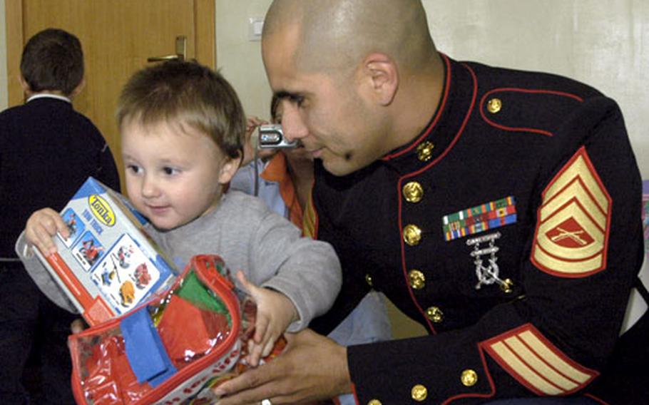 Gunnery Sgt. Carlos Flores hands 2-year-old Salvatore a few gifts Tuesday as part of the Toys for Toys holiday campaign. Marines and sailors from the Naples, Italy, area collected thousands and thousands of toys from donors, which are being distributed to 28 area charities, schools and churches for underprivileged children.