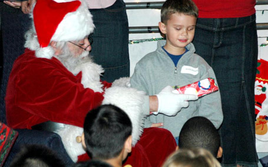 Four-year-old Alex Dickerson gets a Christmas present from Santa Claus at holiday party Monday for the families of deployed servicemembers at the Yokota Airmen and Family Readiness Center.