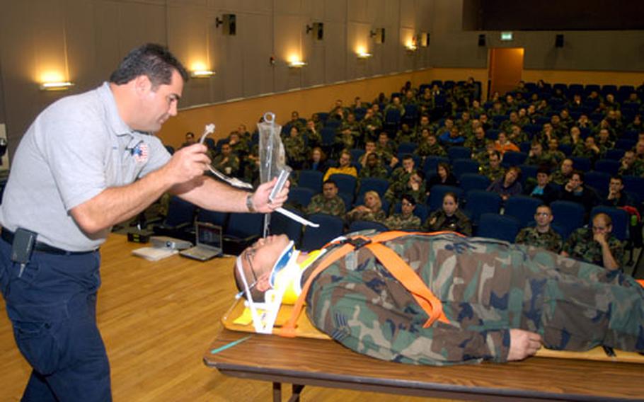 Joe McCluan, a teacher for the Florida-based Stay Alive From Education program, shows audience members a breathing apparatus as Senior Airman Lawrence Dojoles plays the role of a trauma victim during a presentation at the RAF Mildenhall theater.