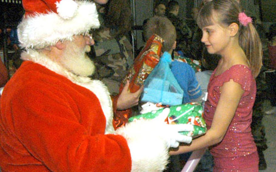 Dressed as Santa, Norman Killen, a British civilian with the 48th Equipment Maintenance Squadron, hands a gift to 8-year-old Skye Marsh inside the American Air Museum last week. Seventy local children were invited to attend a Christmas party sponsored by the maintenance squadron and the 48th Munitions Squadron.