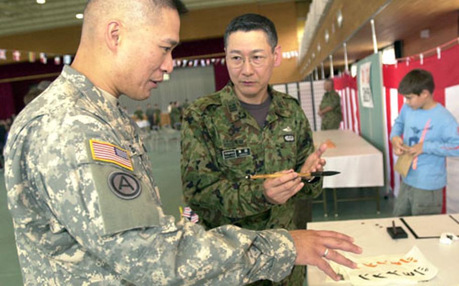 Army Maj. Roy Banzon, left, with the 505th Quartermaster Battalion, listens as Japanese Ground Self-Defense Force Lt. Col. Taneo Hamada, a dentist with 1st Combined Brigade, explains that the symbols he used to write Banzon&#39;s name in calligraphy could also be translated as "much respect." Banzon, who plans to frame the parchment, said, "I didn&#39;t realize that was what (my name) meant."