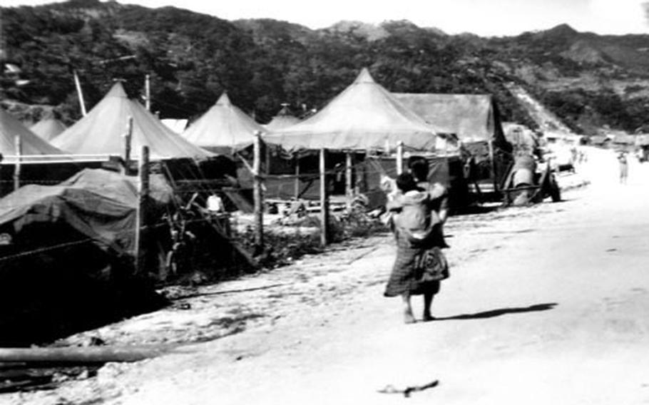 A barefoot mother carries her child past rows of refugee tents on Okinawa in 1945. The photo is one of a box full of photographs donated to an Okinawa historical society by American veteran Robert Rock.