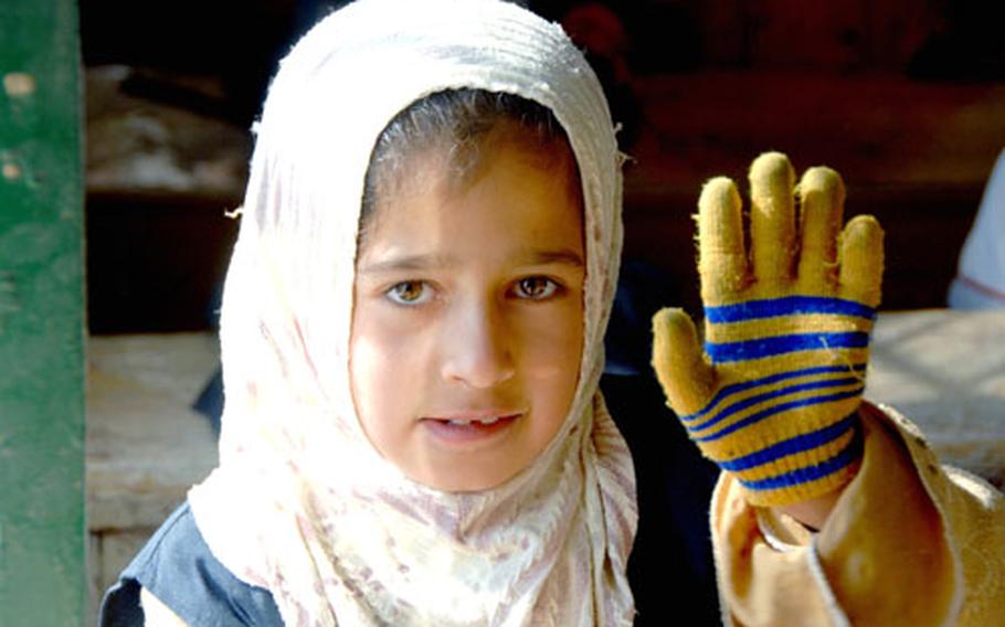 An Iraqi schoolgirl waves at the camera during class at the primary school adopted by 9th Engineer Support Battalion. There is no power in the building, so most of the children wear tattered gloves and hats to stay warm during their lessons. The Marines plan to hook up a generator so the school can have heat.