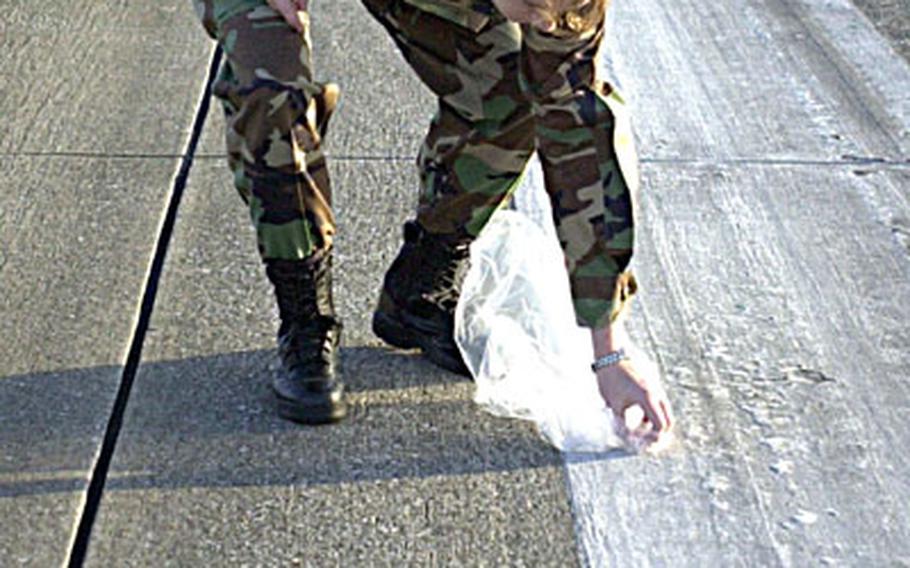 Capt. Lynette Conley, 38, from Portland, Ore., with 31st Rescue Squadron, uses her trash bag to scoop up snails, pebbles, rocks and any other debris on Kadena Air Base&#39;s two-and-a-half mile long runway during its annual FOD walk.