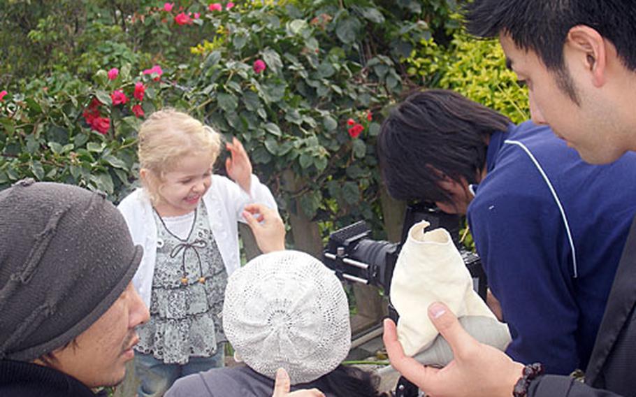Three-year-old Odessa Fredericks giggles as a stylist tweaks her appearance Friday, before the start of a photo shoot in a neighborhood near Gate 2 Street. Most of the crew speaks only Japanese, but a translator from the casting agency Fredericks is signed with is always on hand, said her mother, Suzie Fredericks.