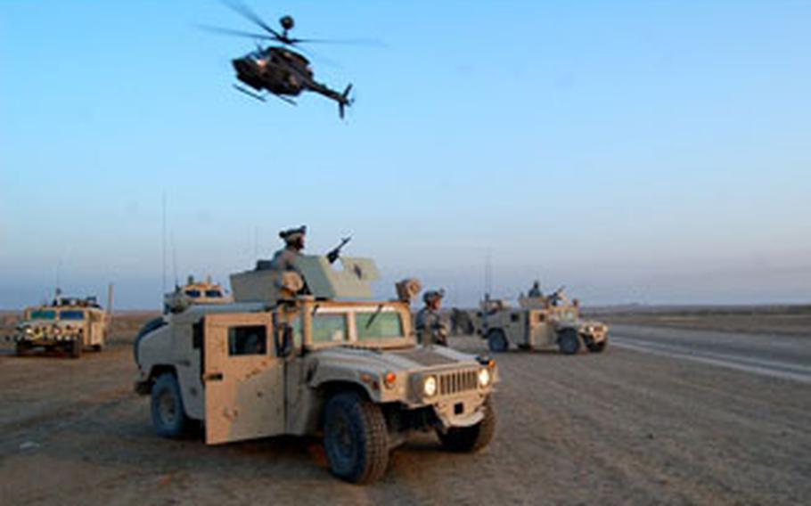 Ground forces of 2nd Battalion, 35th Infantry Regiment, 25th Infantry Division, stage outside of a village in the Rashaad Valley as a team of OH-58D Kiowa Warriors fly overhead.