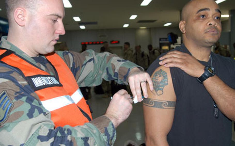 Staff Sgt. Jason Peters, noncommissioned officer in charge of the Misawa Air Base allergy and immunization clinic, gives a last-minute shot to Tech. Sgt. Charles Cox Jr. Wednesday morning at the base passenger terminal. Cox was among about 100 Misawa airmen who departed Wednesday for a 4-month deployment to Iraq.