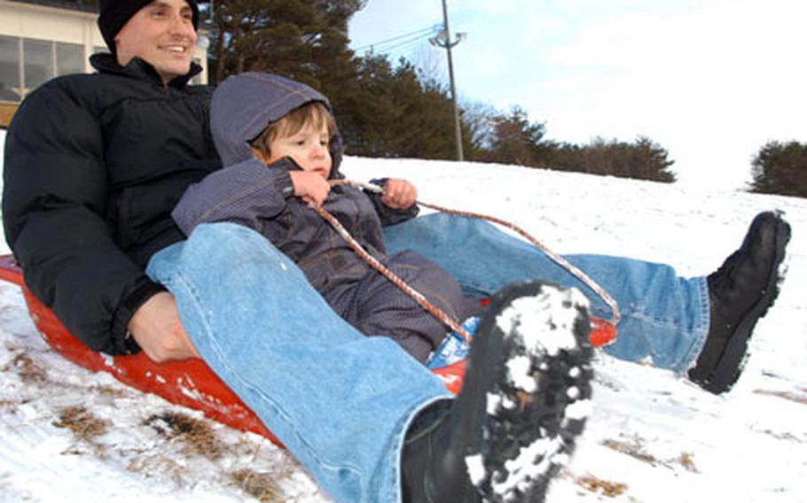 Petty Officer 1st Class Gary Rose points downhill with 3-year-old son, Isaac, Friday afternoon at the Misawa Air Base ski lodge. A 3-inch accumulation overnight Thursday barely covered the hill, but despite the grassy spots, was just enough for some speedy sledding.
