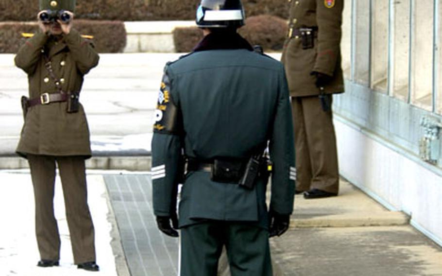 A South Korean guard stands near the demarcation line separating the Koreas while two North Korean guards keep a close eye on members of the press assembled for the historic 3,000th meeting of the Neutral Nations Supervisory Commission on Tuesday at Panmunjom.